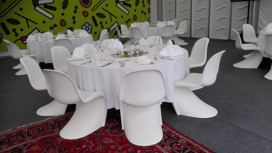 Yritysjuhlien kalusteet: pyöreät pöydät, valkoiset pöytäliinat, banquet tuolit ja valkoiset stretch tuolihameet.